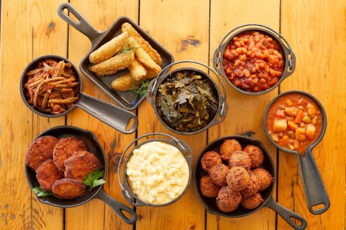 A variety of Southern dishes in cast iron skillets, including fried okra, collard greens, baked beans, and cornbread.