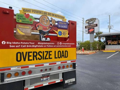 A truck promoting Idaho potatoes parked near a restaurant, featuring an oversized load sign and colorful branding.