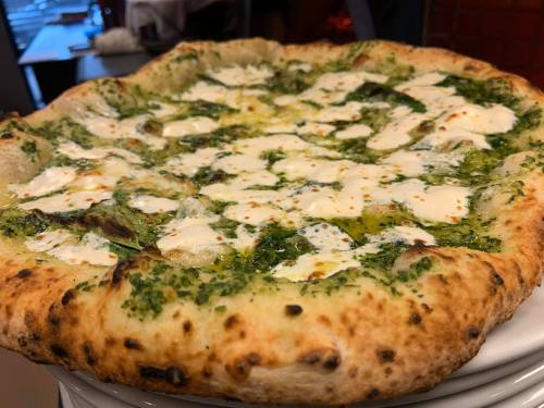A close-up of a freshly baked pizza topped with green pesto, mozzarella, and a golden crust.