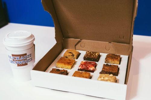 A box of assorted brownies with a coffee cup beside it, all on a white surface.