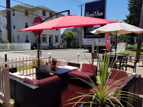 Outdoor seating area with umbrellas, plants, and a sign for Rosso Vino on a sunny day.