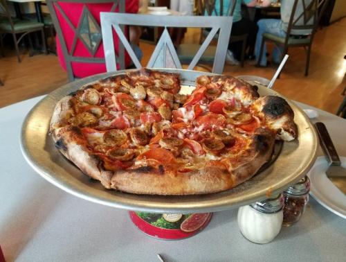 A large pizza topped with pepperoni and sausage on a metal serving tray, placed on a table in a restaurant.