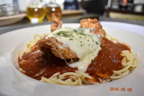 A plate of spaghetti topped with marinara sauce, fried chicken, and melted cheese, garnished with herbs.