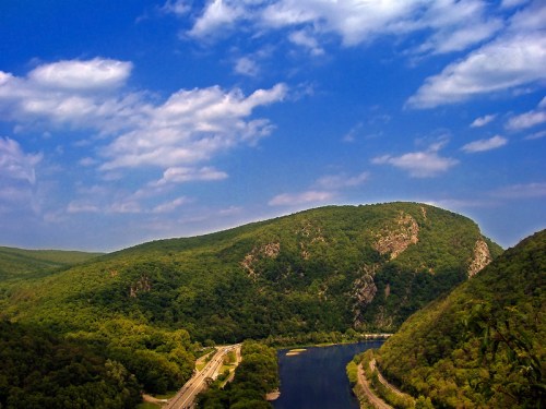 A scenic view of a river winding through lush green hills under a blue sky with fluffy clouds.