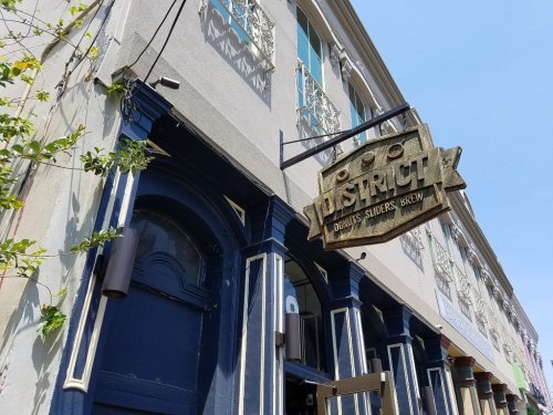 Sign for "District" restaurant with a blue entrance and decorative building facade under a clear blue sky.