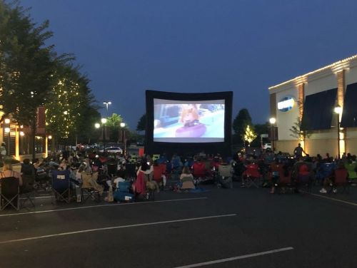 Outdoor movie screening at night with a large inflatable screen and an audience seated in lawn chairs.