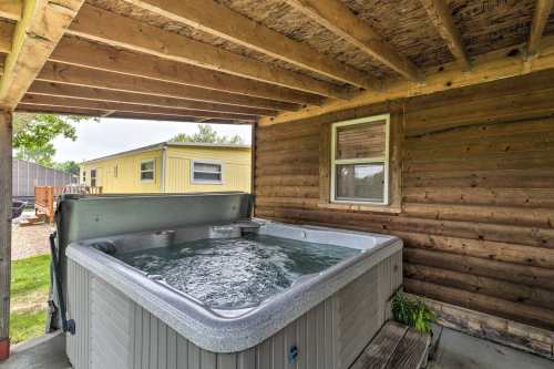 A hot tub under a wooden structure, with a view of a grassy area and nearby buildings.