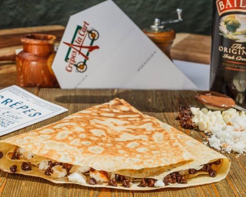 A delicious crepe filled with chocolate chips and white chocolate, served with a menu and a bottle of Baileys.