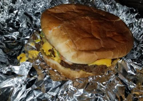 A cheeseburger with melted cheese and toppings, wrapped in foil, resting on a shiny surface.