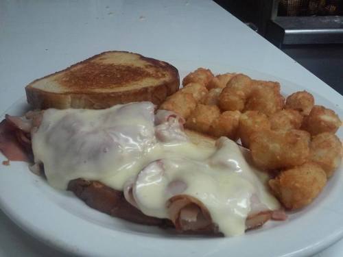 A plate of melted cheese over ham, served with toast and crispy tater tots.
