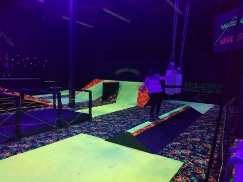 A vibrant indoor trampoline park with neon ramps and colorful flooring, featuring a person jumping on a trampoline.