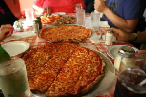A table with two large pizzas and drinks, surrounded by people enjoying a meal together.