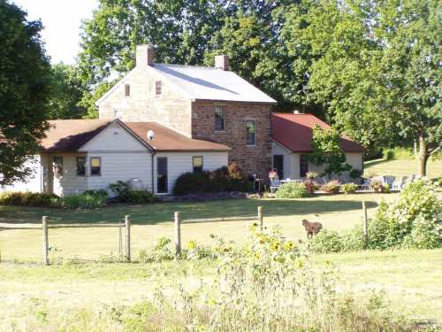 A charming two-story house with a mix of stone and wood siding, surrounded by greenery and a garden.