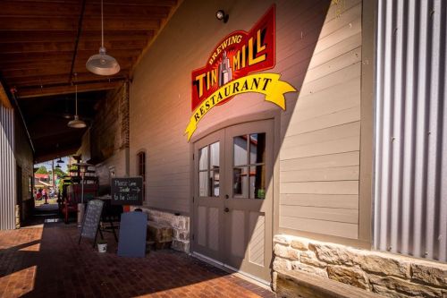 Exterior view of the Tin Mill Restaurant, featuring a sign and entrance with rustic architecture and a brick pathway.