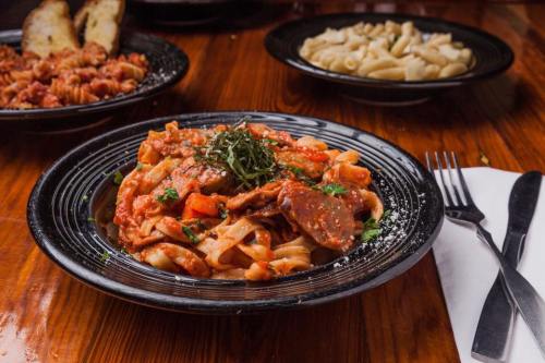 A plate of pasta with sausage and tomato sauce, garnished with herbs, on a wooden table with other dishes in the background.