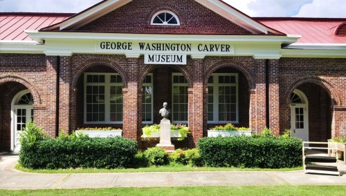 Exterior of the George Washington Carver Museum, featuring a brick facade, large windows, and a statue in front.