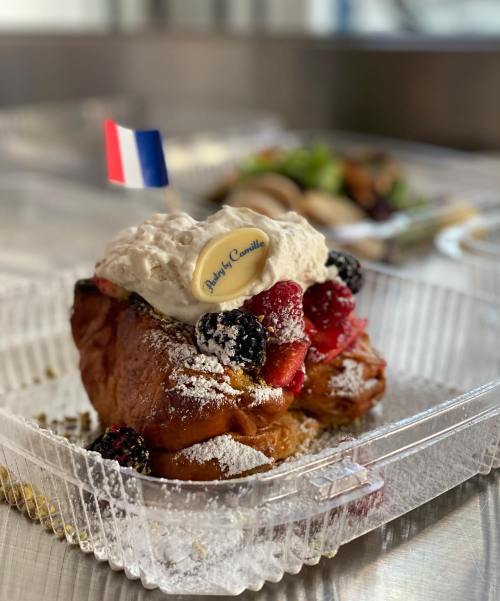 A delicious pastry topped with whipped cream, berries, and a decorative flag, served in a clear container.