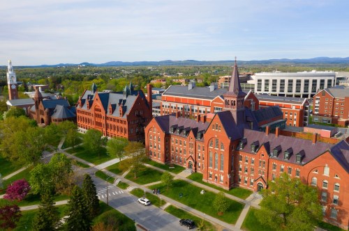 Aerial view of a college campus featuring historic red brick buildings and green trees under a clear blue sky.
