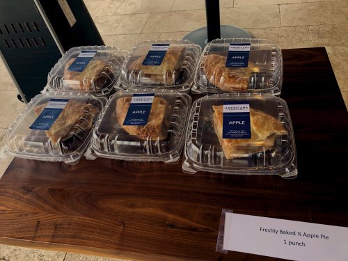 Six containers of freshly baked apple pie on a wooden table, labeled "Freshly Baked ¼ Apple Pie, 1 punch."