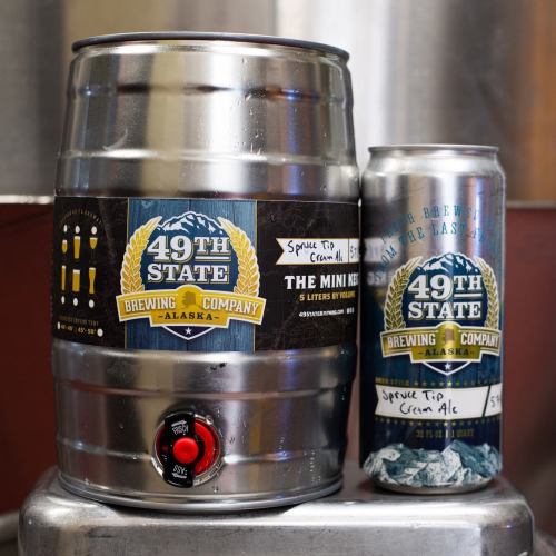 A mini keg and can of 49th State Brewing Company's Spruce Tip Cream Ale, featuring branding and a tap handle.