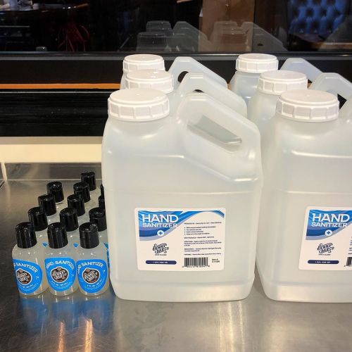 Several large containers of hand sanitizer next to smaller bottles on a countertop.