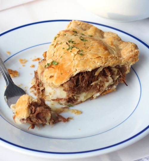 A slice of savory meat pie on a plate, with flaky crust and a fork beside it.