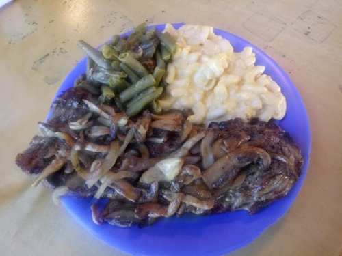 A blue plate with grilled meat topped with onions, green beans, and macaroni and cheese.