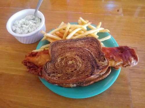 A plate with a sandwich on toasted bread, crispy bacon, fries, and a small bowl of coleslaw.