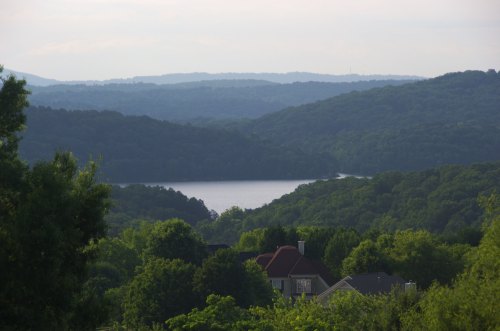 A serene landscape featuring rolling green hills, a calm lake, and distant mountains under a soft sky.