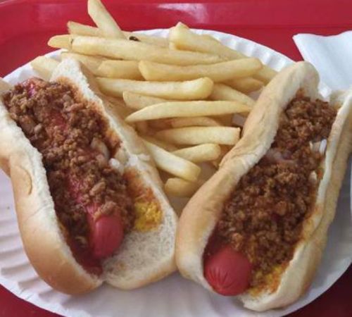 Two hot dogs topped with chili and onions, served with a side of golden French fries on a white plate.