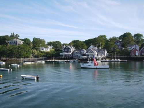 A peaceful harbor scene with a boat flying an American flag and charming houses along the shore.