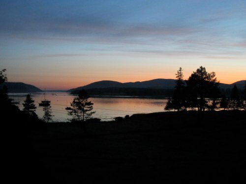 A serene sunset over a calm lake, with silhouettes of trees and mountains in the background.