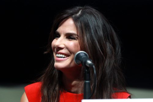 A woman in a red dress smiles brightly while sitting at a microphone during a panel discussion.