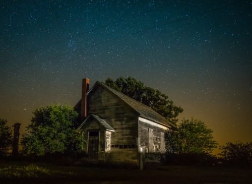 An old, abandoned house under a starry night sky, surrounded by trees and a serene atmosphere.