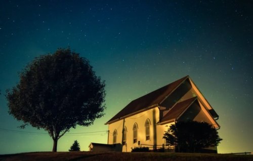 A serene night scene featuring a church and a tree under a starry sky, illuminated softly by ambient light.