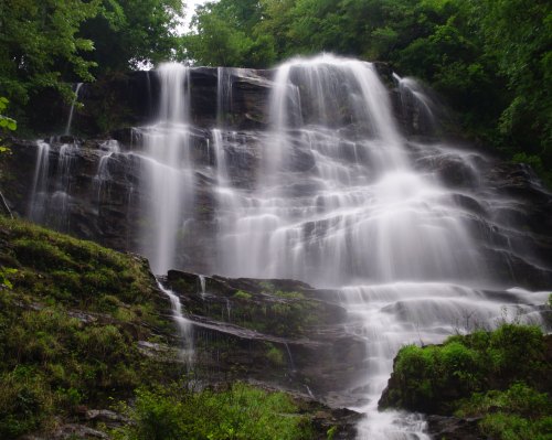 A cascading waterfall flows down rocky cliffs, surrounded by lush green foliage.