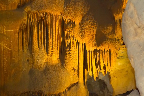 Stalactites and rock formations illuminated in a cave, showcasing textures and warm lighting.