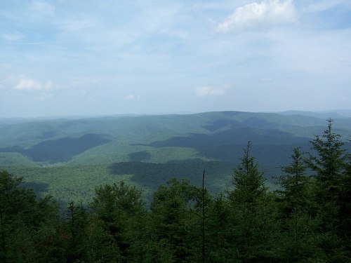 A panoramic view of rolling green mountains under a blue sky with scattered clouds.
