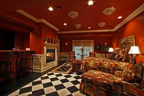 Cozy living room with orange walls, floral furniture, a fireplace, and a checkered floor. Warm lighting enhances the ambiance.