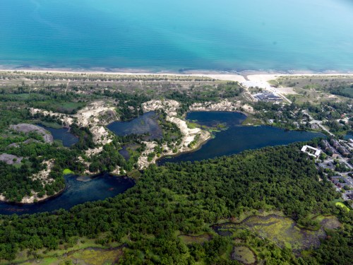 Aerial view of a coastal landscape featuring a lake, sandy beach, and lush greenery along the shoreline.