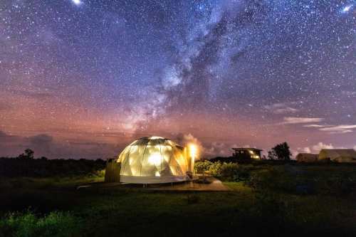 A geodesic dome under a starry sky, with the Milky Way visible and soft lights illuminating the structure.
