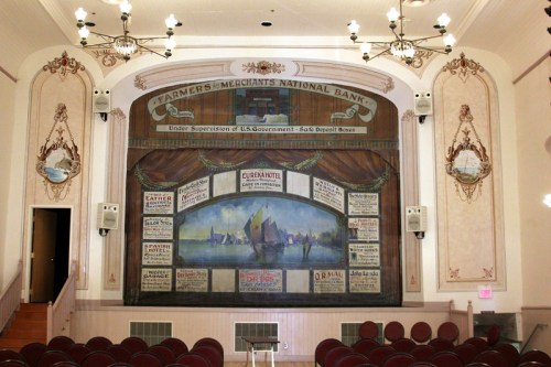 Interior of a historic theater featuring a decorative mural and stage with vintage advertisements and ornate details.