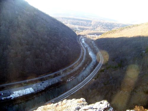 A winding river flows between two mountains, with a road and parking area visible below in a scenic landscape.