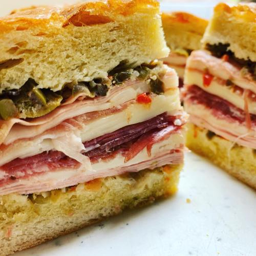 Close-up of a sliced sandwich with layers of meats, cheese, and pickles on a soft bread.