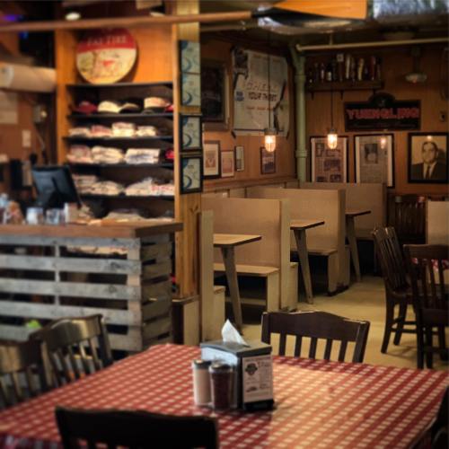 Cozy restaurant interior with wooden tables, booths, and a checkered tablecloth, featuring vintage decor and a bar area.