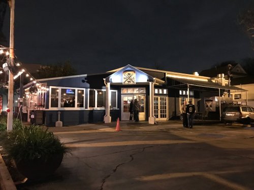 A blue and white restaurant at night, with outdoor seating and string lights, and people gathered outside.