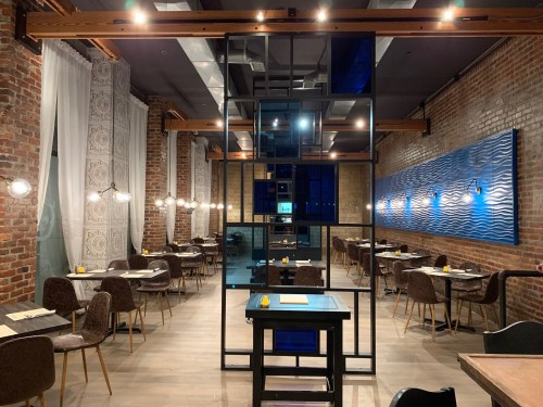 Modern restaurant interior with brick walls, wooden accents, and tables set for dining under warm lighting.