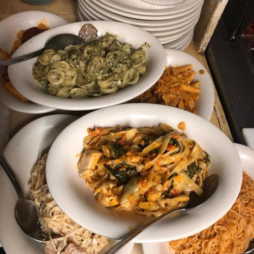 A variety of pasta dishes served in white bowls, including orecchiette, penne, and fettuccine, with sauces and vegetables.