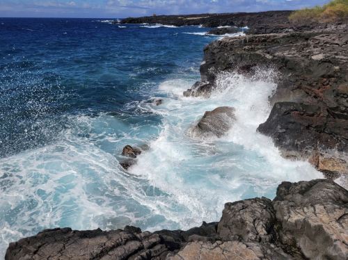 Waves crash against rocky coastline under a bright blue sky, creating a dynamic seascape.
