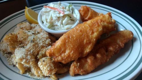 A plate of fried fish fillets, creamy macaroni and cheese, and coleslaw, garnished with a lemon wedge.